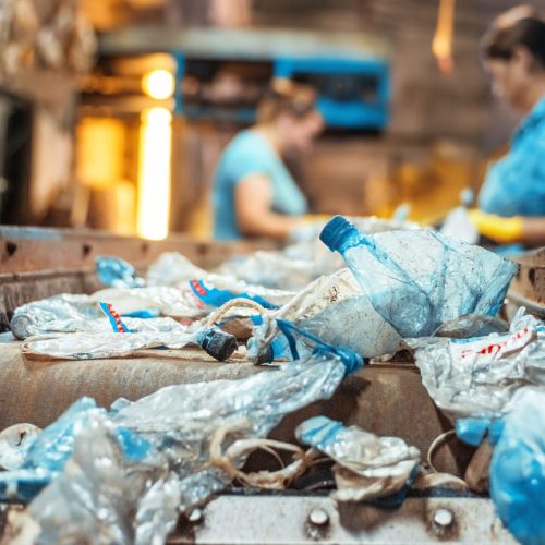 Plastic garbage on a conveyor belt at waste recycling factory. Workers on the background